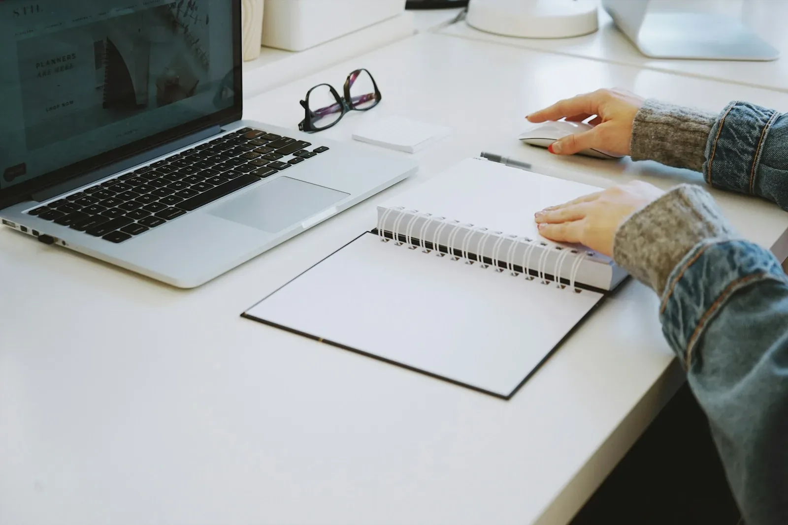 Une main posée sur un carnet à spirale, à côté d’un ordinateur